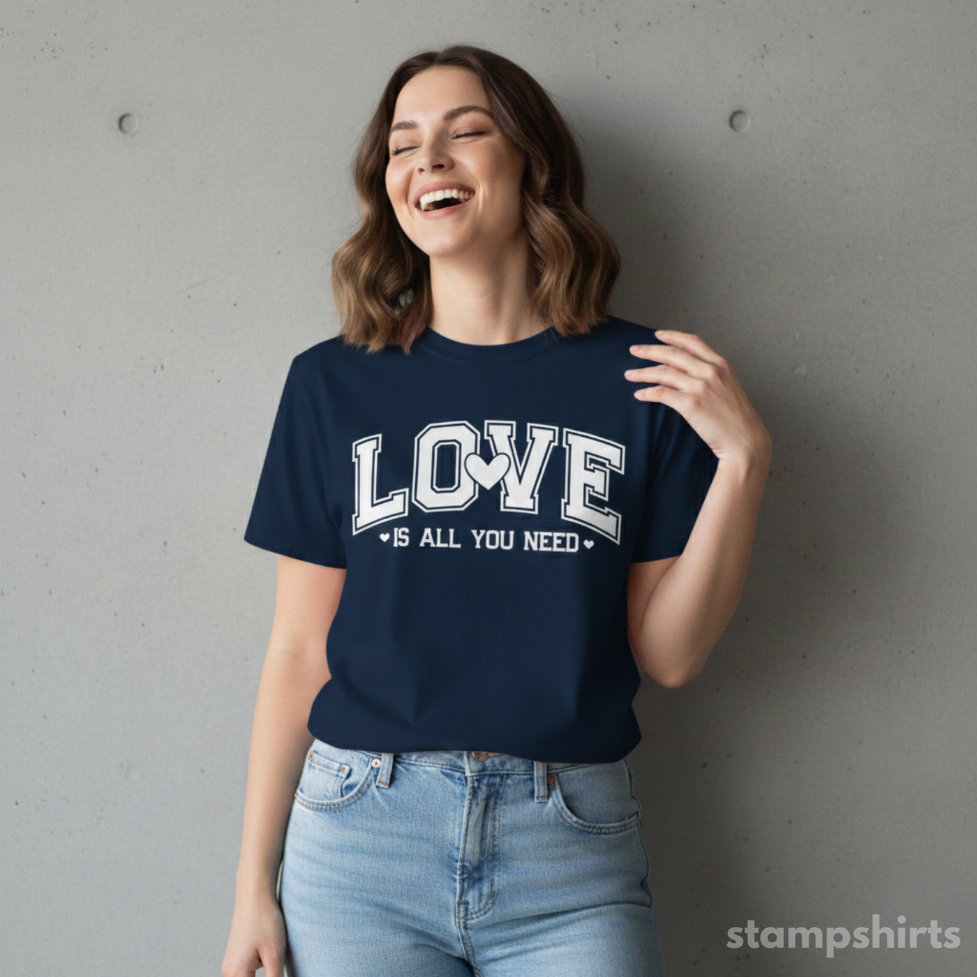 Woman wearing a navy blue t-shirt with 'LOVE is all you need' text, standing against a gray wall. image 4