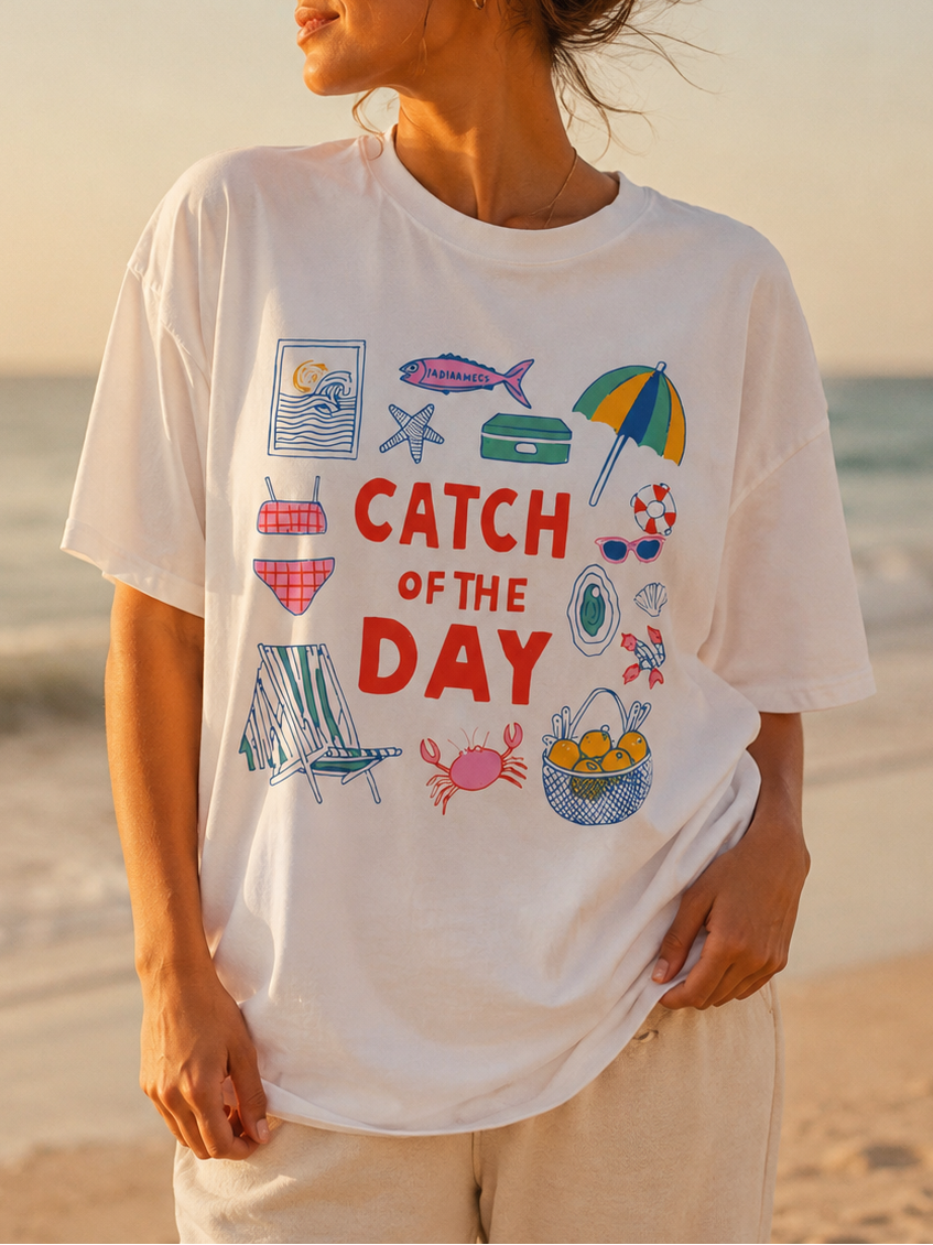 Woman wearing a 'Catch of the Day' t-shirt on a beach at sunset