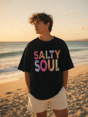 Person wearing a black t-shirt with 'Salty Soul' on a beach at sunset