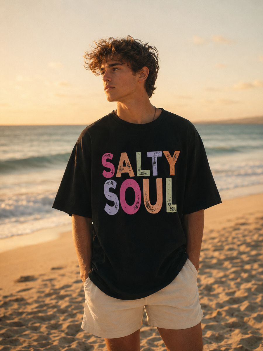 Person wearing a black t-shirt with 'Salty Soul' on a beach at sunset
