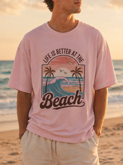 Man wearing a pink t-shirt with a beach graphic and text on a beach at sunset.