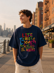 Person wearing a navy blue t-shirt with colorful text, standing on a city street with buildings and water in the background.