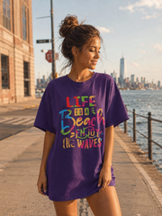 Woman wearing a purple t-shirt with colorful text by a waterfront with a city skyline.