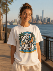 Person wearing a 'Don't Be Salty' t-shirt by a waterfront with a city skyline in the background