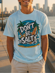 Man wearing a 'Don't Be Salty' t-shirt by a waterfront with a city skyline in the background