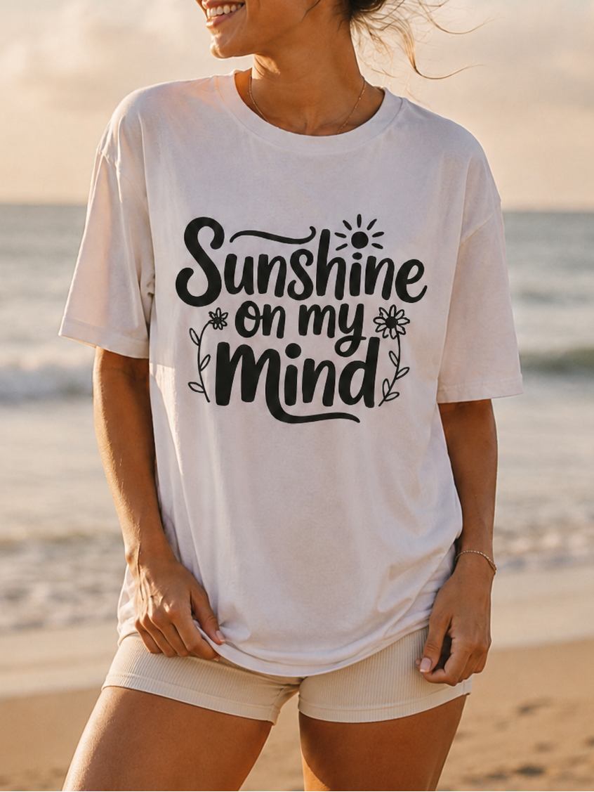 Woman wearing a white t-shirt with 'Sunshine on my Mind' text at the beach.
