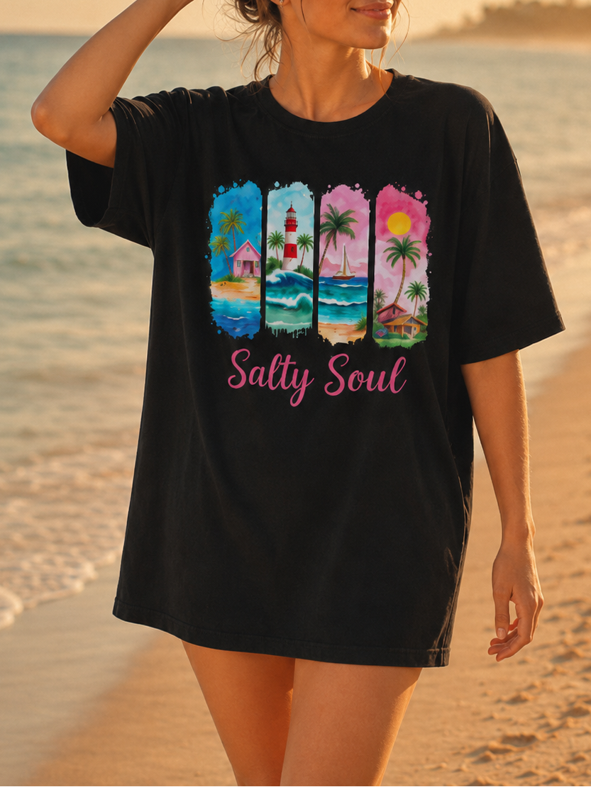 Woman wearing a black t-shirt with colorful graphics and text on a beach at sunset.