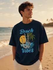 Man wearing a 'Beach Vibes' t-shirt on a beach with palm trees and a sunset.