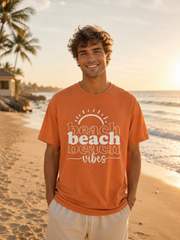 Man wearing an orange 'beach vibes' t-shirt on a beach at sunset.