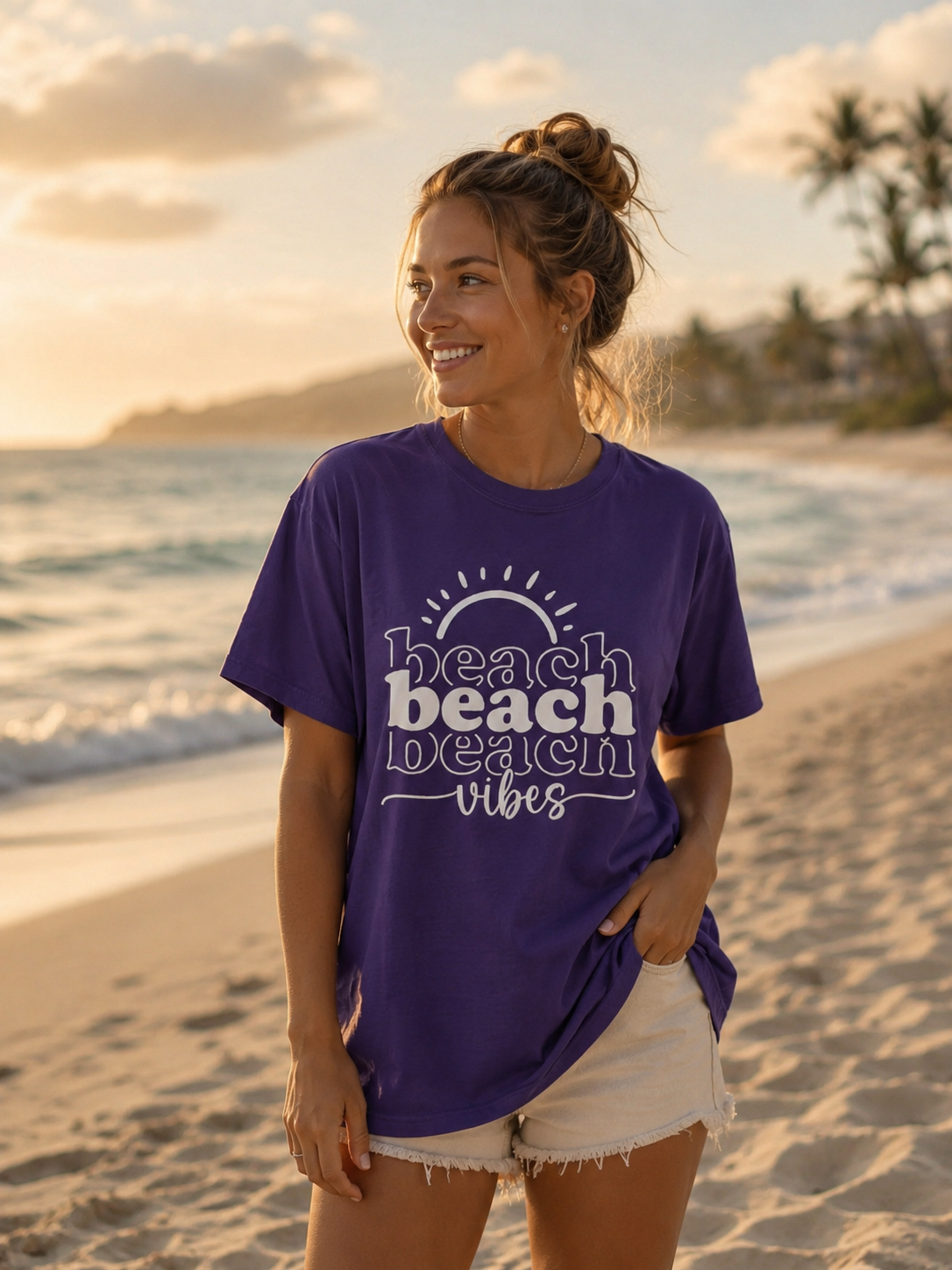 Woman wearing a purple 'beach vibes' t-shirt on a beach at sunset.