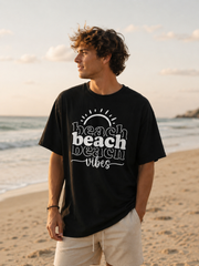 Man wearing a black t-shirt with 'beach vibes' text on a beach at sunset.
