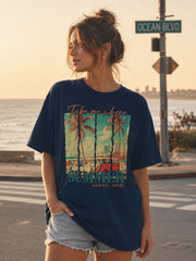 Woman wearing a navy blue t-shirt with a beach graphic and text by the ocean.
