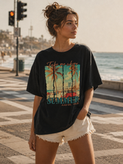 Woman wearing a black t-shirt with a colorful graphic and text, standing on a coastal street.