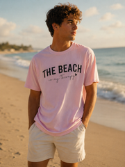Man wearing a pink t-shirt with 'The Beach is my Therapy' text on a beach.