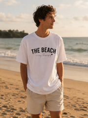 Man wearing a white t-shirt with 'The Beach is my Therapy' on a beach at sunset.