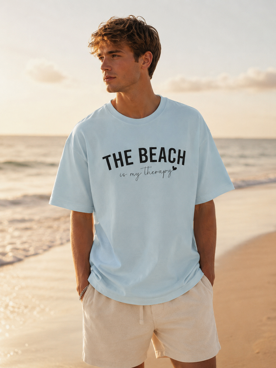 Man wearing a light blue t-shirt with 'THE BEACH is my Therapy' text on a beach.