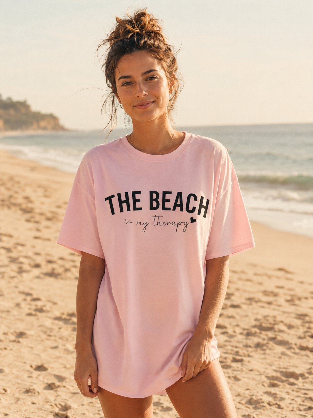 Woman wearing a pink t-shirt with 'The Beach is my Therapy' text on a beach.