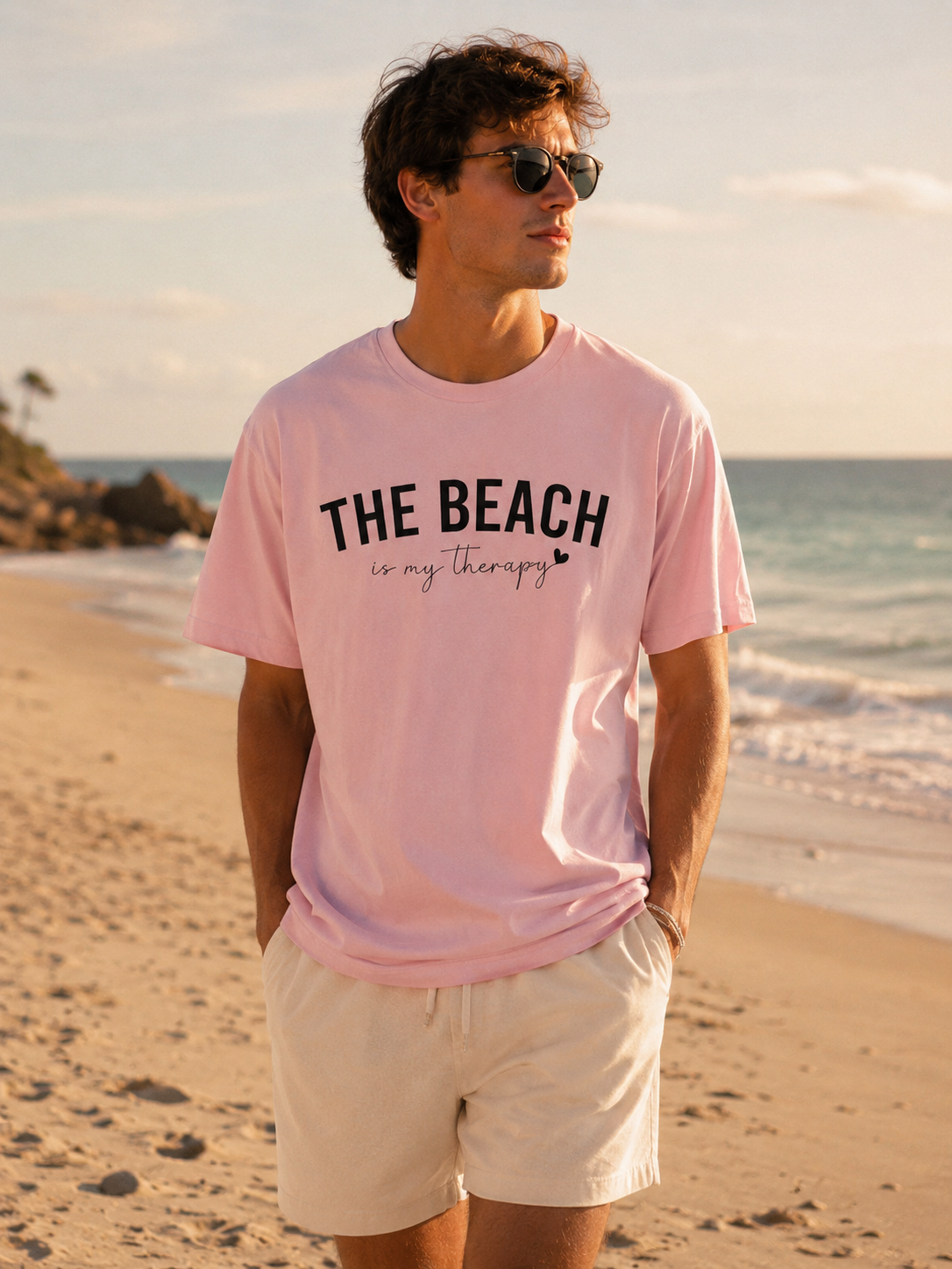 Man wearing a pink t-shirt with 'The Beach is my Therapy' text on a beach.
