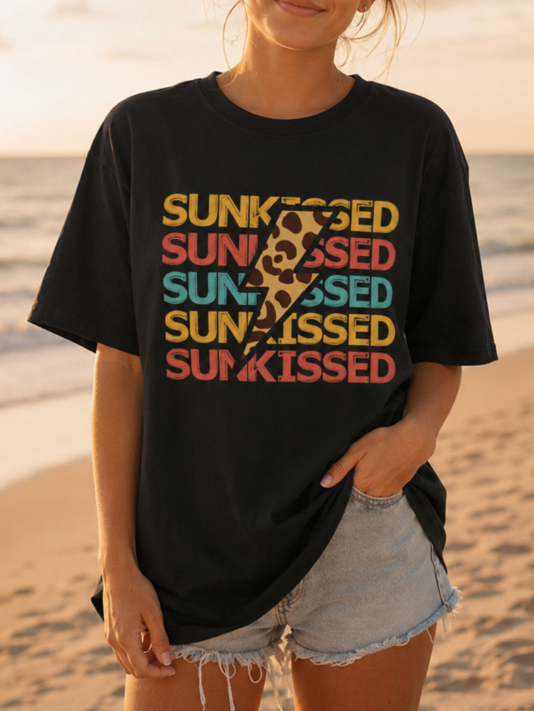 Woman wearing a black t-shirt with colorful text on a beach at sunset
