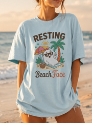 Woman wearing a light blue t-shirt with 'Resting Beach Face' graphic on a beach.