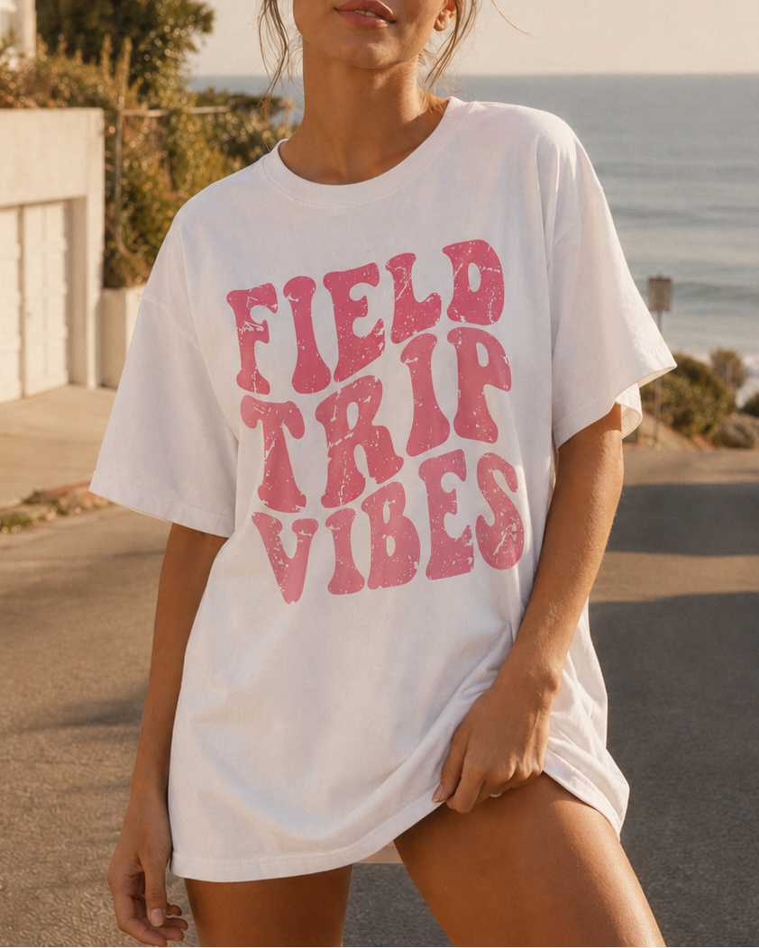 Woman wearing a 'Field Trip Vibes' t-shirt by the ocean.