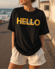 Woman wearing a black t-shirt with 'HELLO sunshine' printed in yellow at the beach.