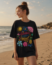 Woman wearing a black t-shirt with colorful graphics and text on a beach.