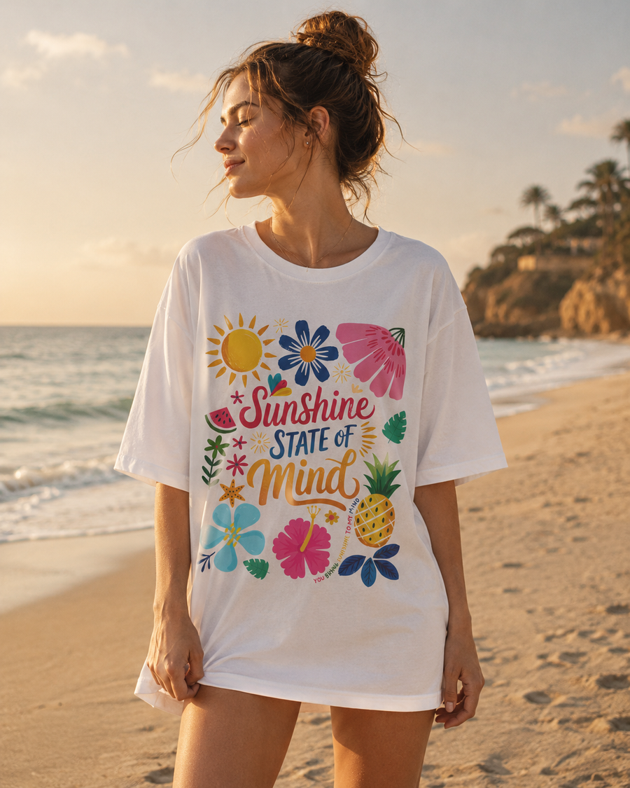 Person wearing a white t-shirt with colorful graphics and text on a beach.