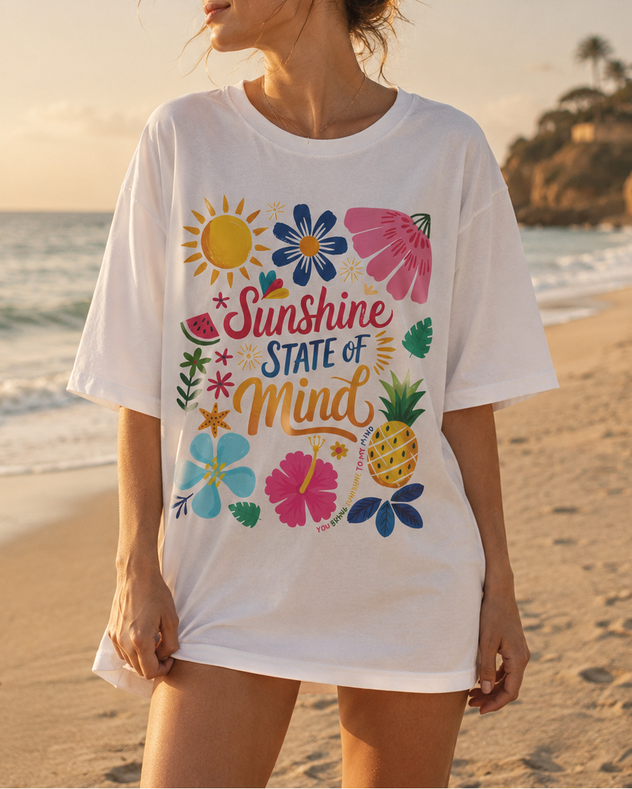 Person wearing a white t-shirt with colorful graphics and text on a beach.
