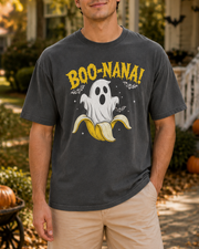A man wearing a dark gray t-shirt with a 'BOO-NANA!' graphic featuring a ghost on a banana, standing outdoors in front of a house decorated for Halloween.