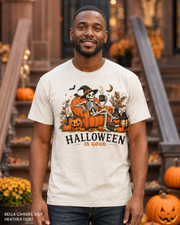 Male model wearing the Bella Canvas 3001 Heather Dust Halloween Is Good skeleton pumpkin chair T-shirt