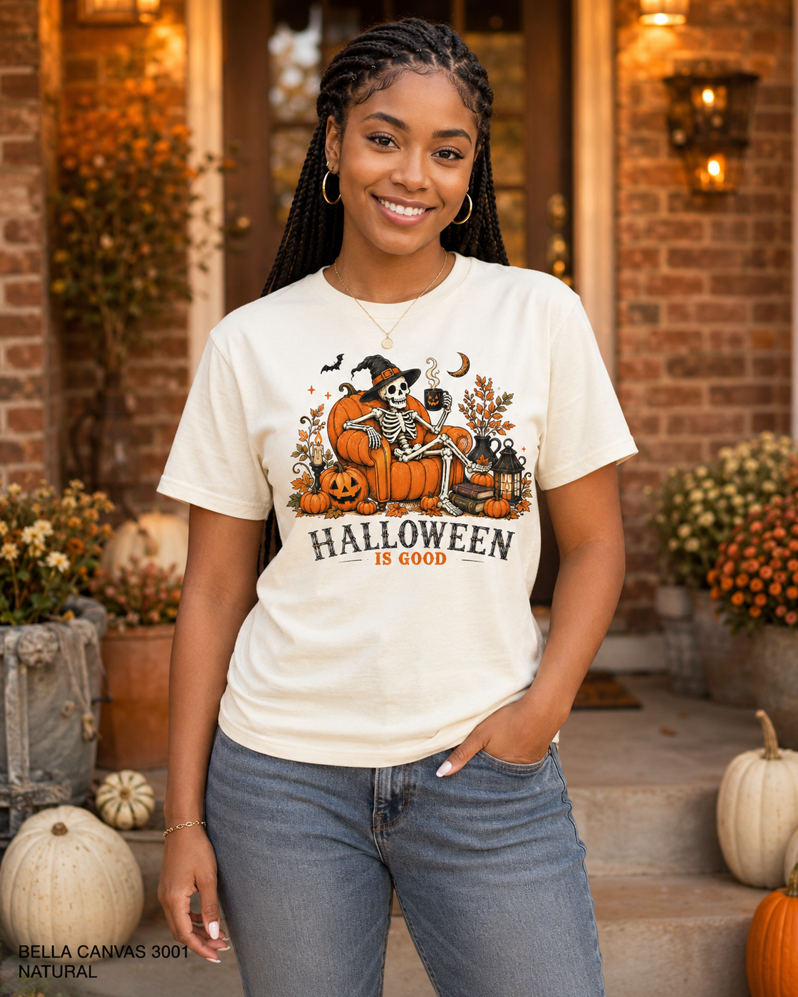 Female model wearing the Bella Canvas 3001 Natural Halloween Is Good skeleton pumpkin chair T-shirt