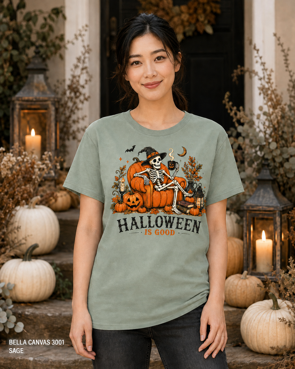 Female model wearing the Bella Canvas 3001 Sage Halloween Is Good skeleton pumpkin chair T-shirt
