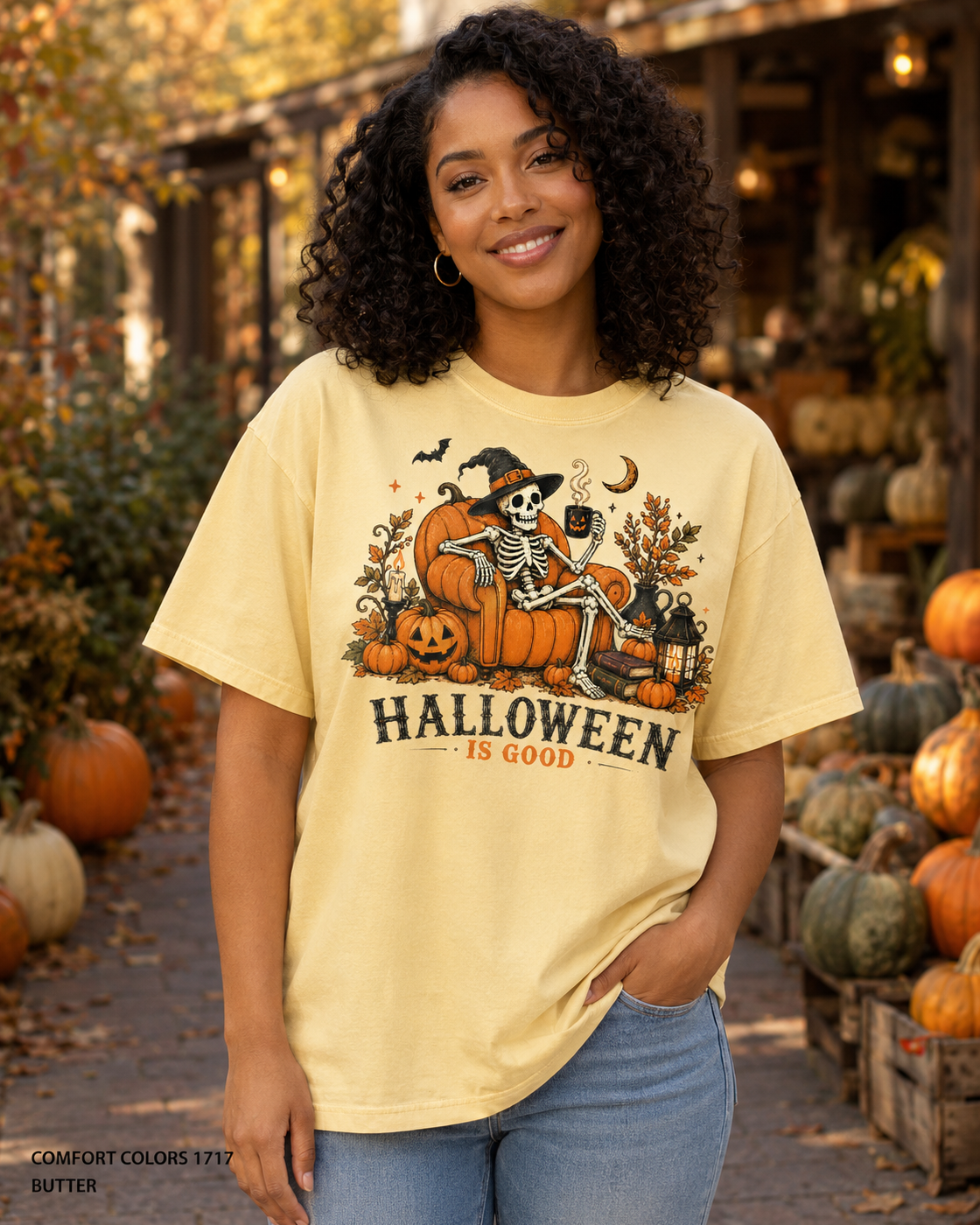 Female model wearing the Comfort Colors 1717 Butter Halloween Is Good skeleton pumpkin chair T-shirt