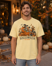 Male model wearing the Comfort Colors 1717 Butter Halloween Is Good skeleton pumpkin chair T-shirt
