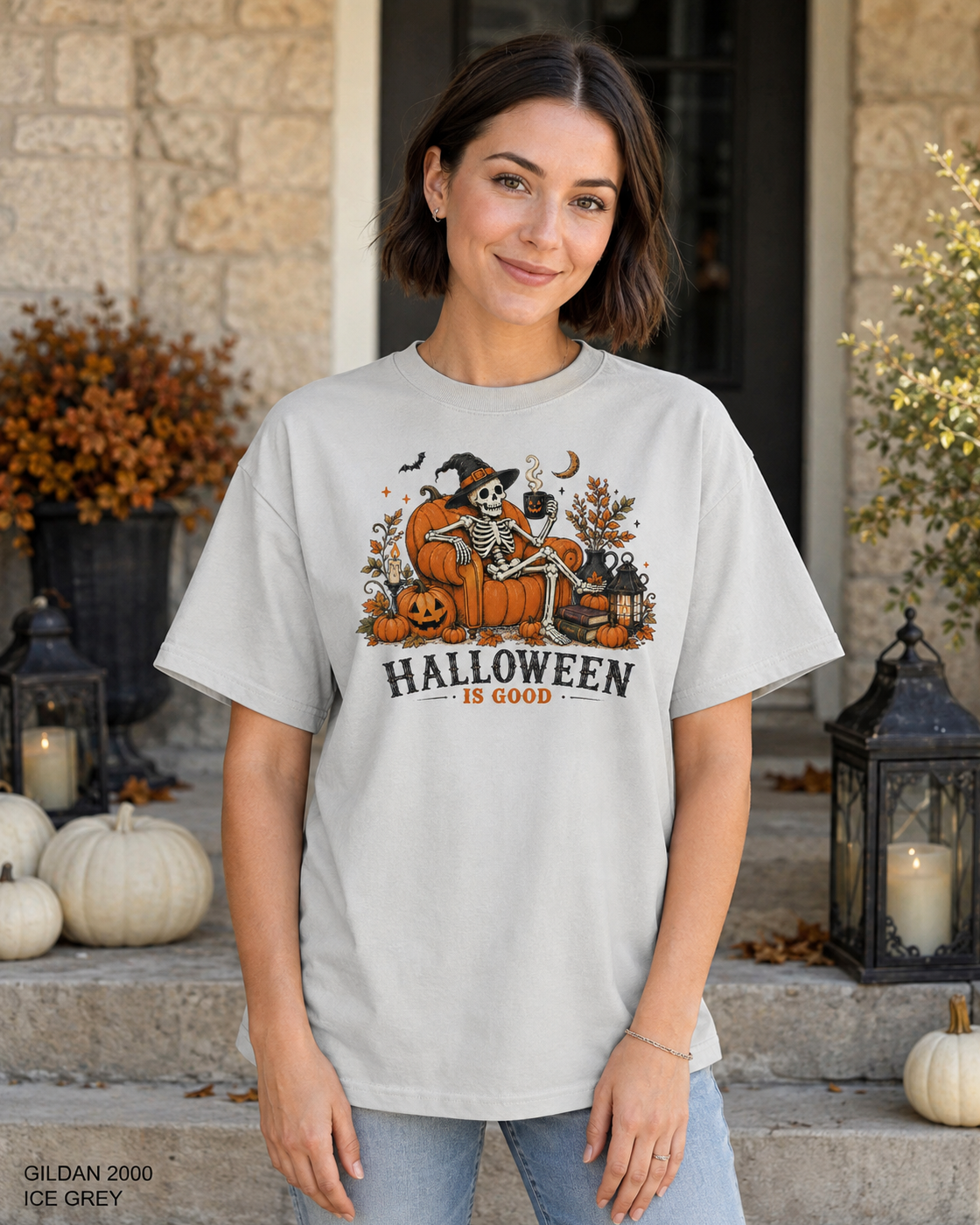 Female model wearing the Gildan 2000 Ice Grey Halloween Is Good skeleton pumpkin chair T-shirt