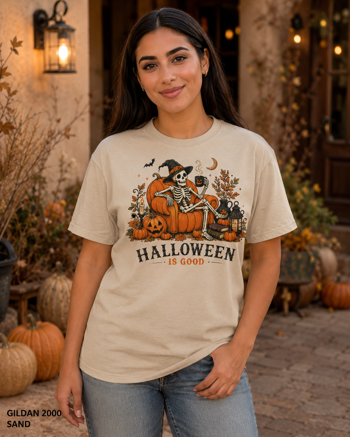 Female model wearing the Gildan 2000 Sand Halloween Is Good skeleton pumpkin chair T-shirt