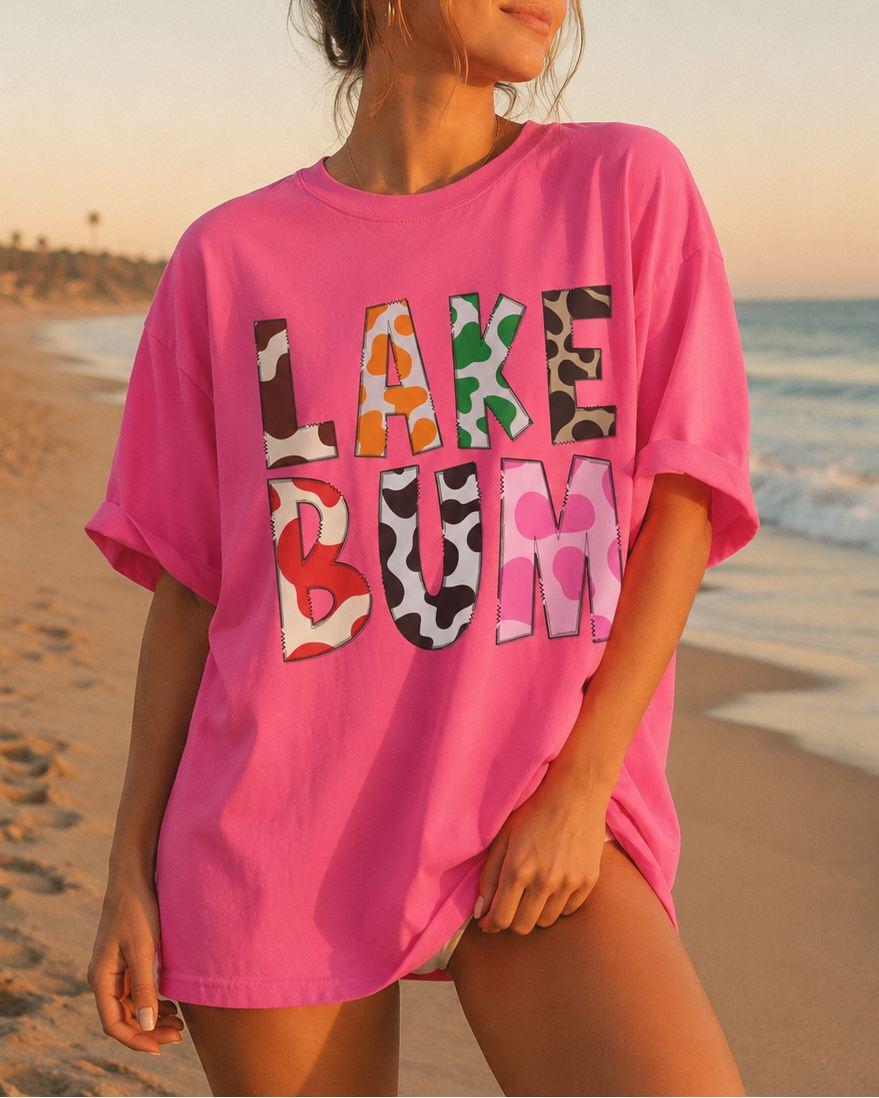 Woman wearing a pink t-shirt with colorful text on a beach at sunset